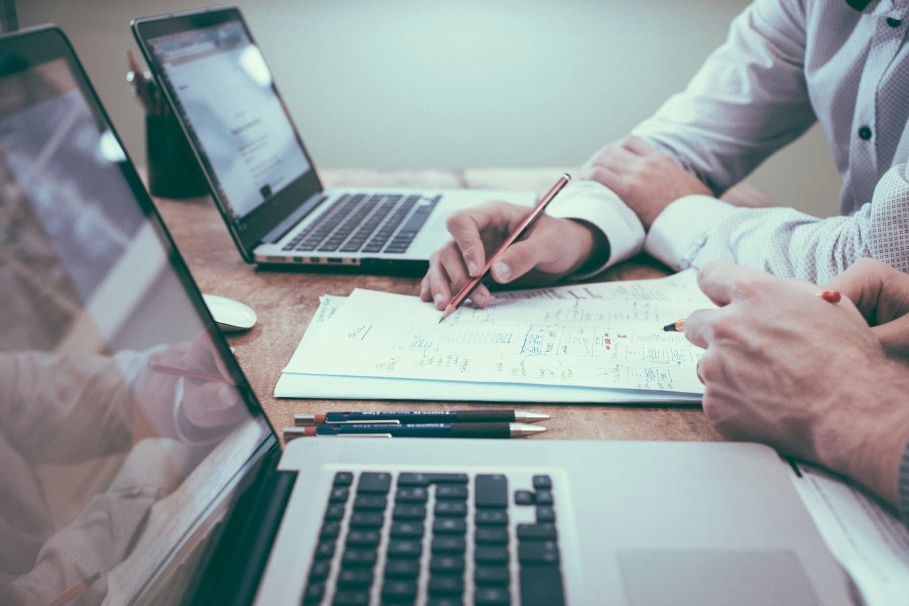 Dos personas revisan planos y cifras en un escritorio, con computadores abiertos, durante una sesión de trabajo.