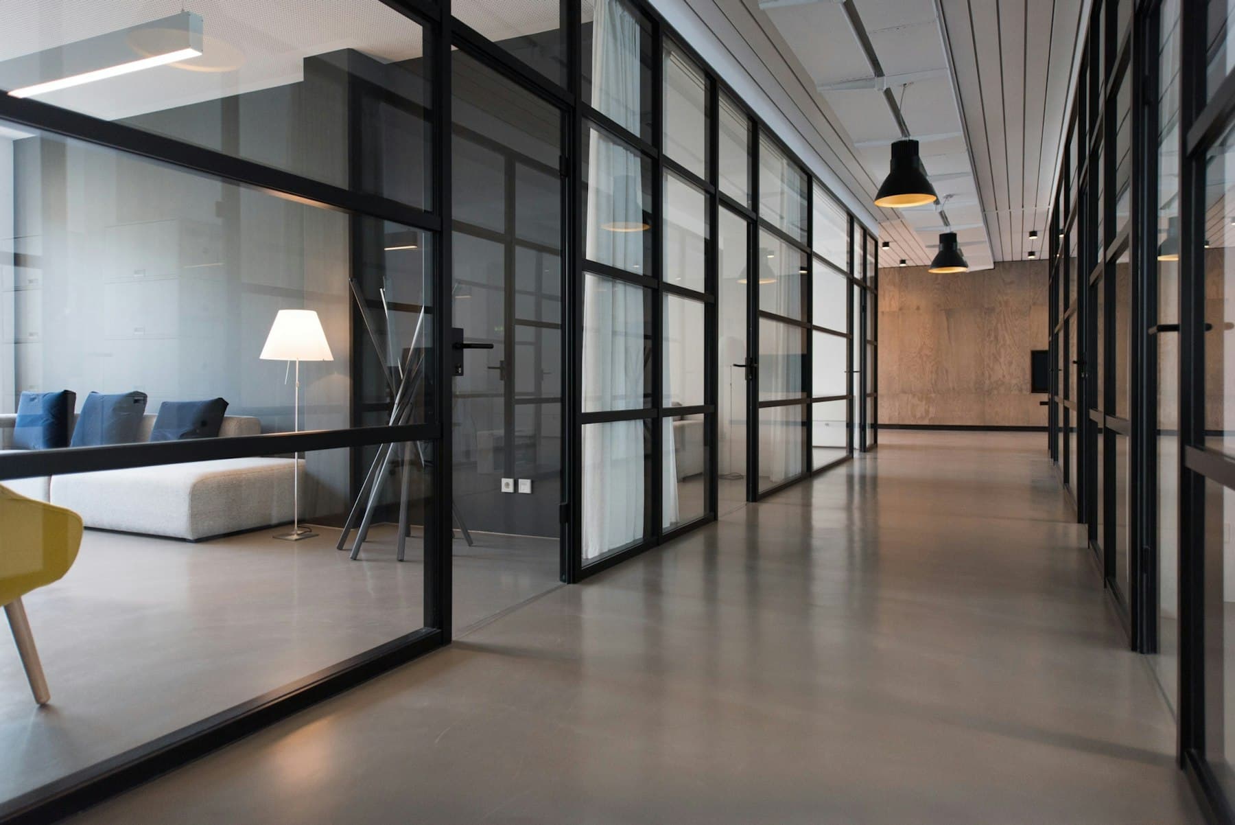Pasillo de una oficina contemporánea con divisiones de vidrio, luz natural y una sala de espera.
